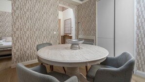 A dining area with a round table and six chairs, a decorative bowl on the table, and patterned wallpaper.