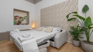 A modern bedroom with a bed, pillows, a bedside lamp, a painting, and potted plants.