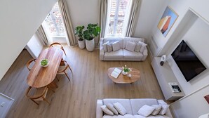 Een ruime woonkamer met een houten eettafel, twee banken en een salontafel. Er staan potplanten en er hangt een schilderij aan de muur.