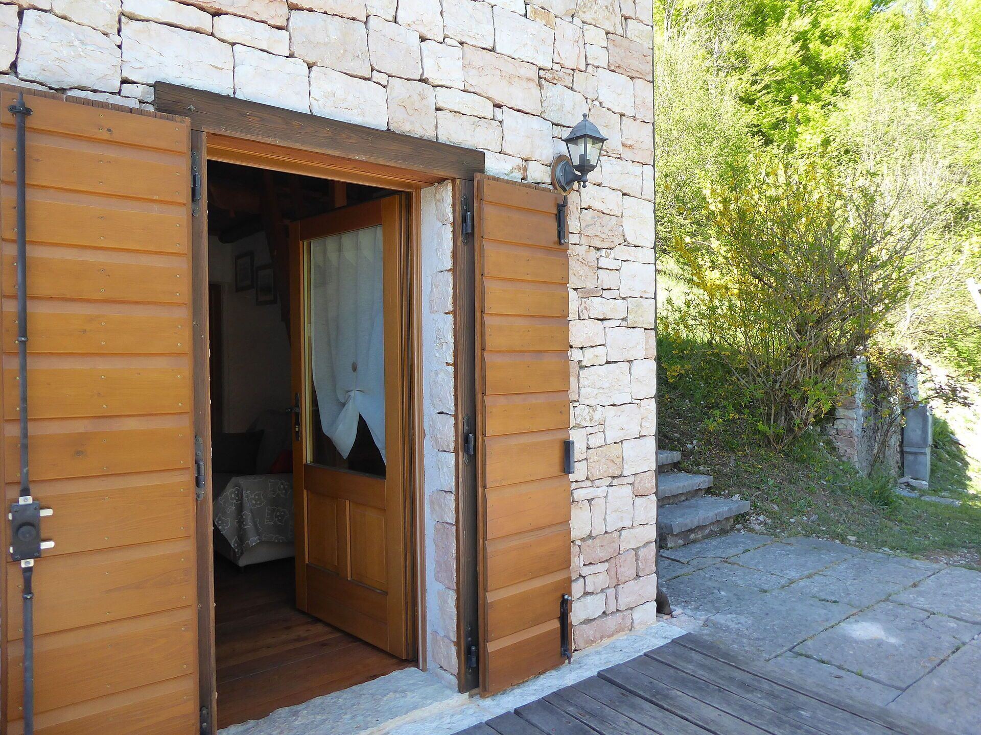 Eine Holztür mit Vorhang, eine Steinmauer und ein kleiner Außenbereich mit Stufen, die zu einem Garten führen.