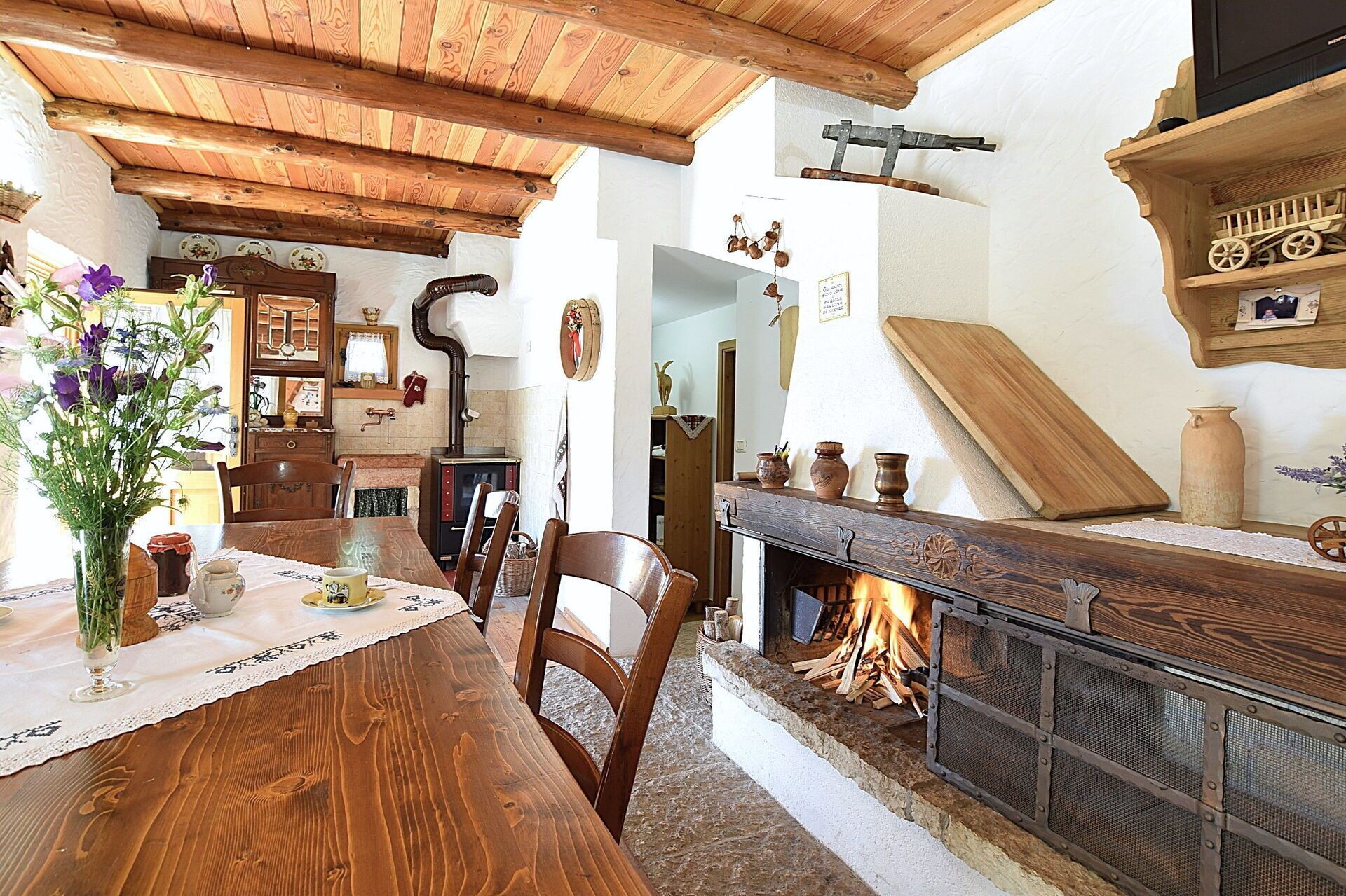 Un interno rustico con un tavolo da pranzo in legno, sedie, un camino e diversi oggetti decorativi.
