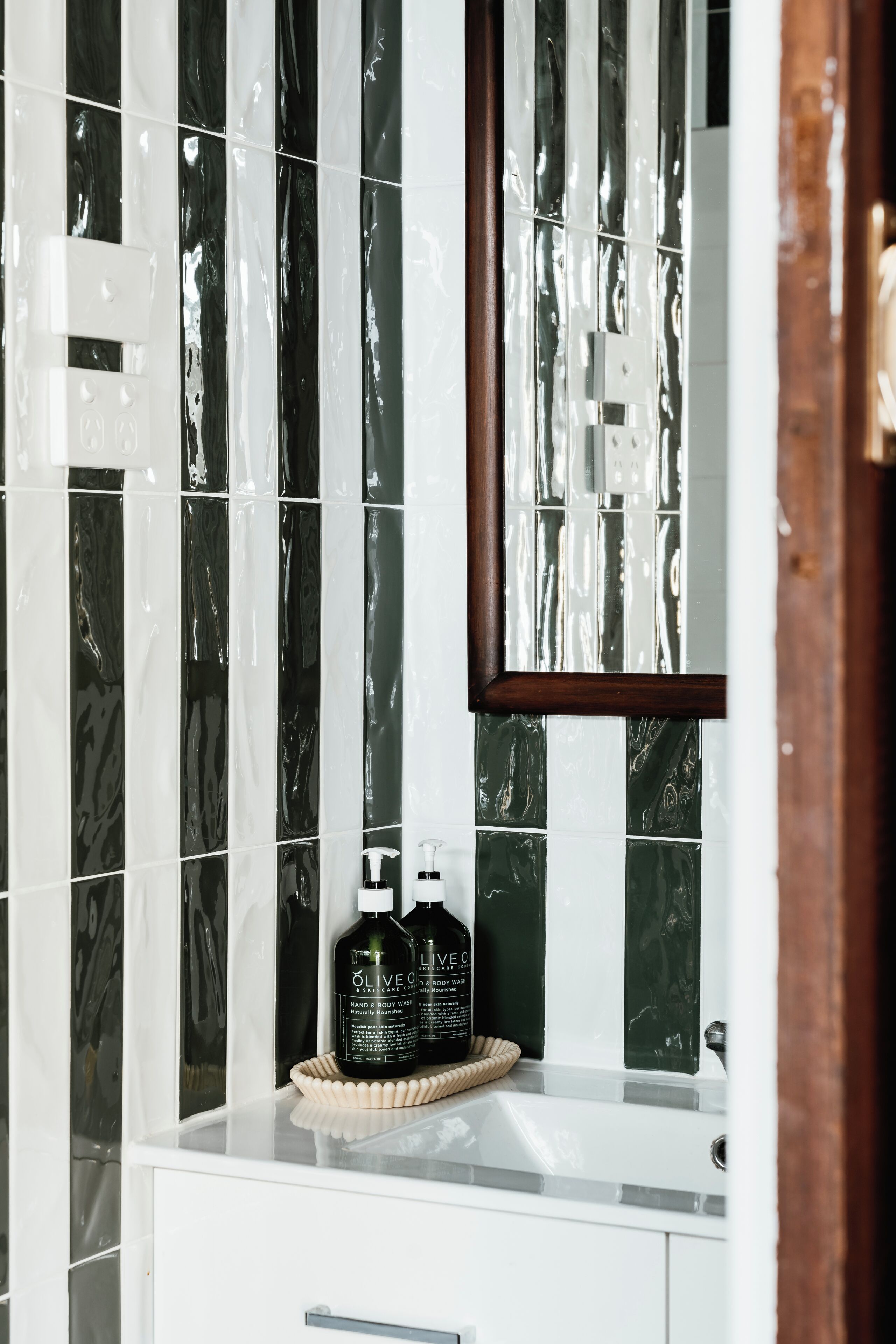 A bathroom with a white sink, a mirror, and two bottles of olive oil on the counter.