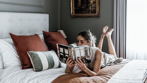 A person lying on a bed in a room with a headboard, pillows, and a painting on the wall. - Benambra Boutique Accommodation (Queenscliff)