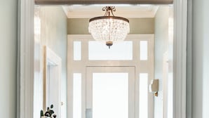 A hallway with a chandelier, a door with a window, and a fire extinguisher. - Benambra Boutique Accommodation (Queenscliff)