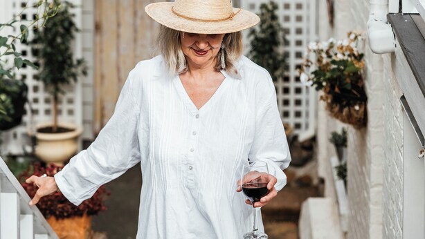 A person in a white dress walking down a narrow alleyway with a white fence on one side and a wooden gate at the end. - Benambra Boutique Accommodation (Queenscliff)