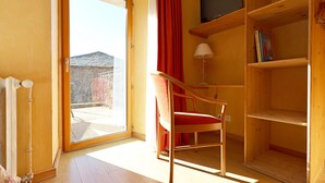 Une pièce avec une porte-fenêtre coulissante, une chaise en bois, une lampe et un téléviseur posé sur une étagère.