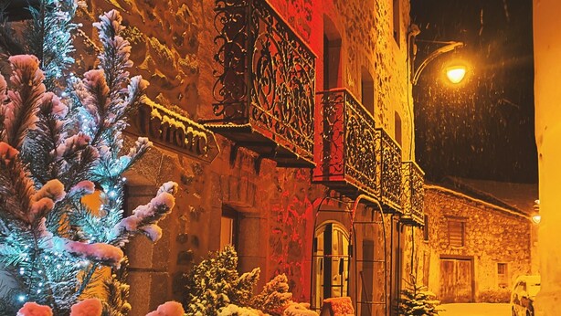 Une rue enneigée, avec un bâtiment orné de balcons travaillés et un lampadaire allumé.