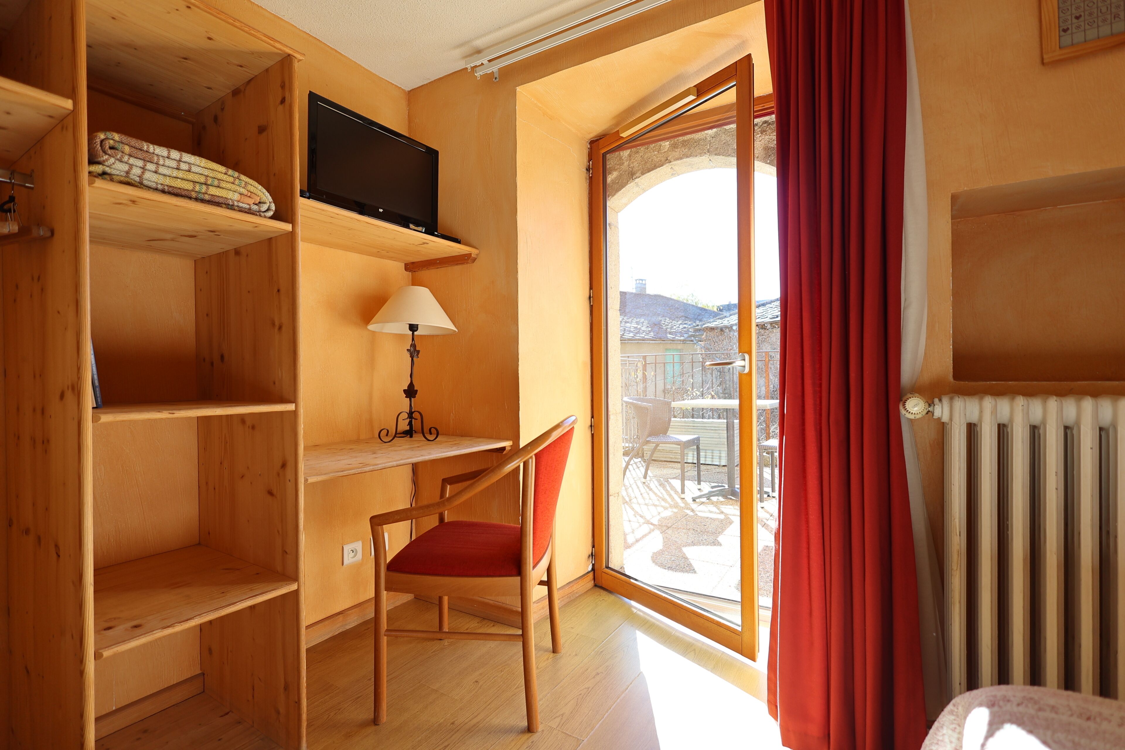A room with a wooden desk, a chair, a television, and a view through a glass door.