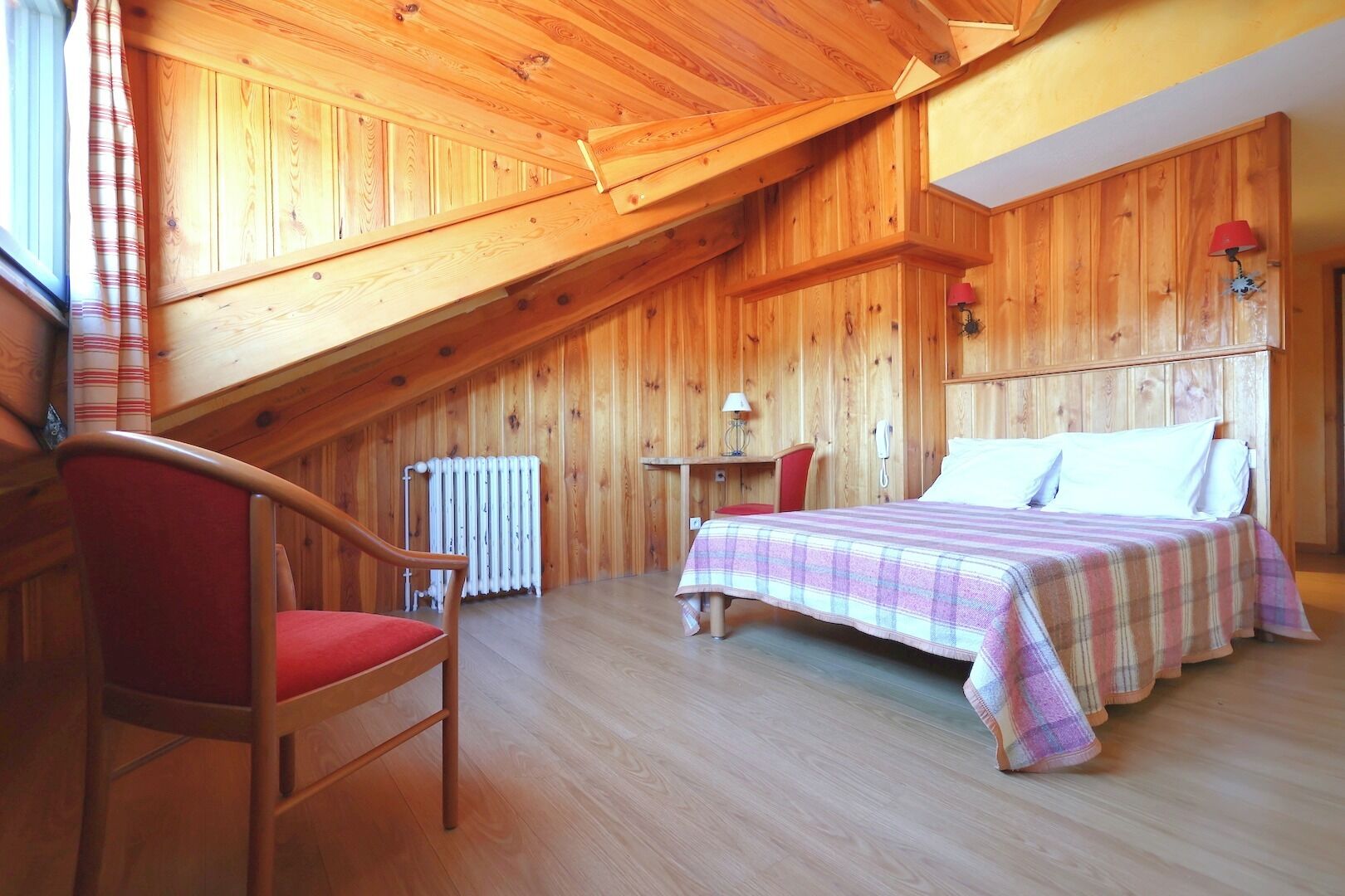 Une pièce en bois avec un lit, une chaise, une table et un radiateur.