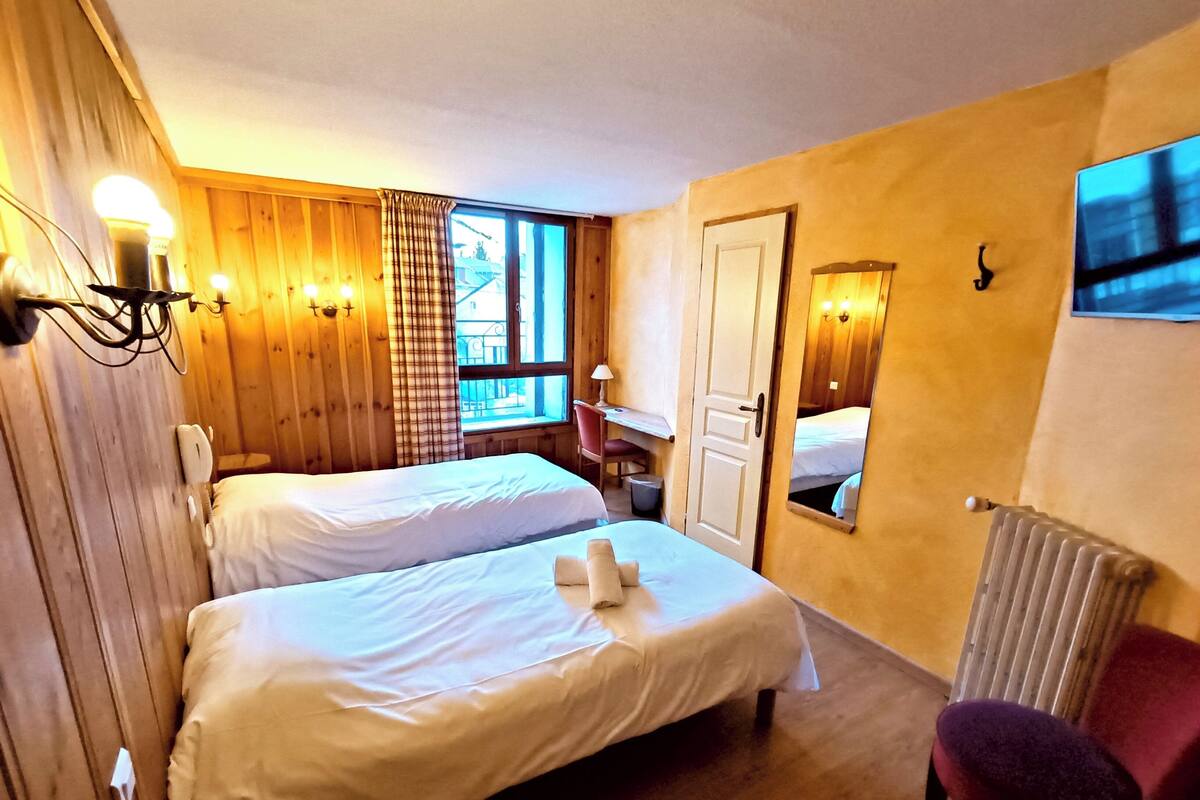 A room with two beds, a desk, a chair, and a radiator.