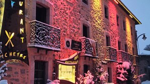 Un hôtel à la façade en pierre, doté d’une enseigne lumineuse et entouré d’un paysage enneigé.