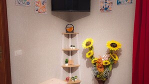 Un salon avec un téléviseur à écran plat fixé au mur, un banc blanc, un grand porte-plantes avec des plantes en pot et un vase rempli de tournesols.