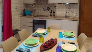Un coin repas avec une table en bois dressée pour quatre personnes, une cuisine en arrière-plan et un rideau rouge sur le côté gauche.