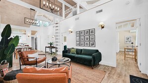 Un vaste espace de vie doté d’un haut plafond, d’un canapé vert, de fauteuils en cuir, d’une table basse et d’un escalier menant à un niveau supérieur.
