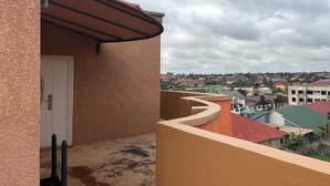 A balcony with a curved wall and a door, overlooking a residential area with various buildings and a cloudy sky. - Charming Pent house 1-bedroom apartment with kitchen, hall and office for a fee (Accra)