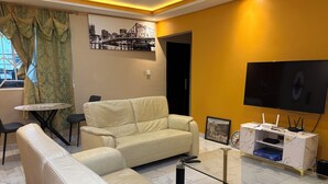 A living room with a sofa, a glass coffee table, a TV, and a framed picture on the wall. - Charming Pent house 1-bedroom apartment with kitchen, hall and office for a fee (Accra)