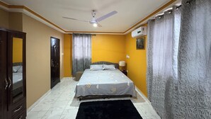 A bedroom with a bed, a ceiling fan, a window with curtains, and a door. - Charming Pent house 1-bedroom apartment with kitchen, hall and office for a fee (Accra)