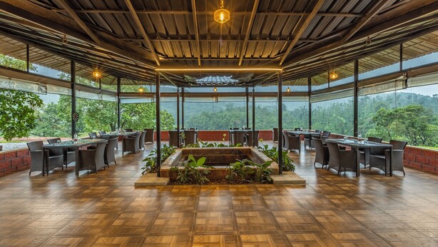 Comedor interior con techo de madera, ventanas amplias y una planta central con vegetación.