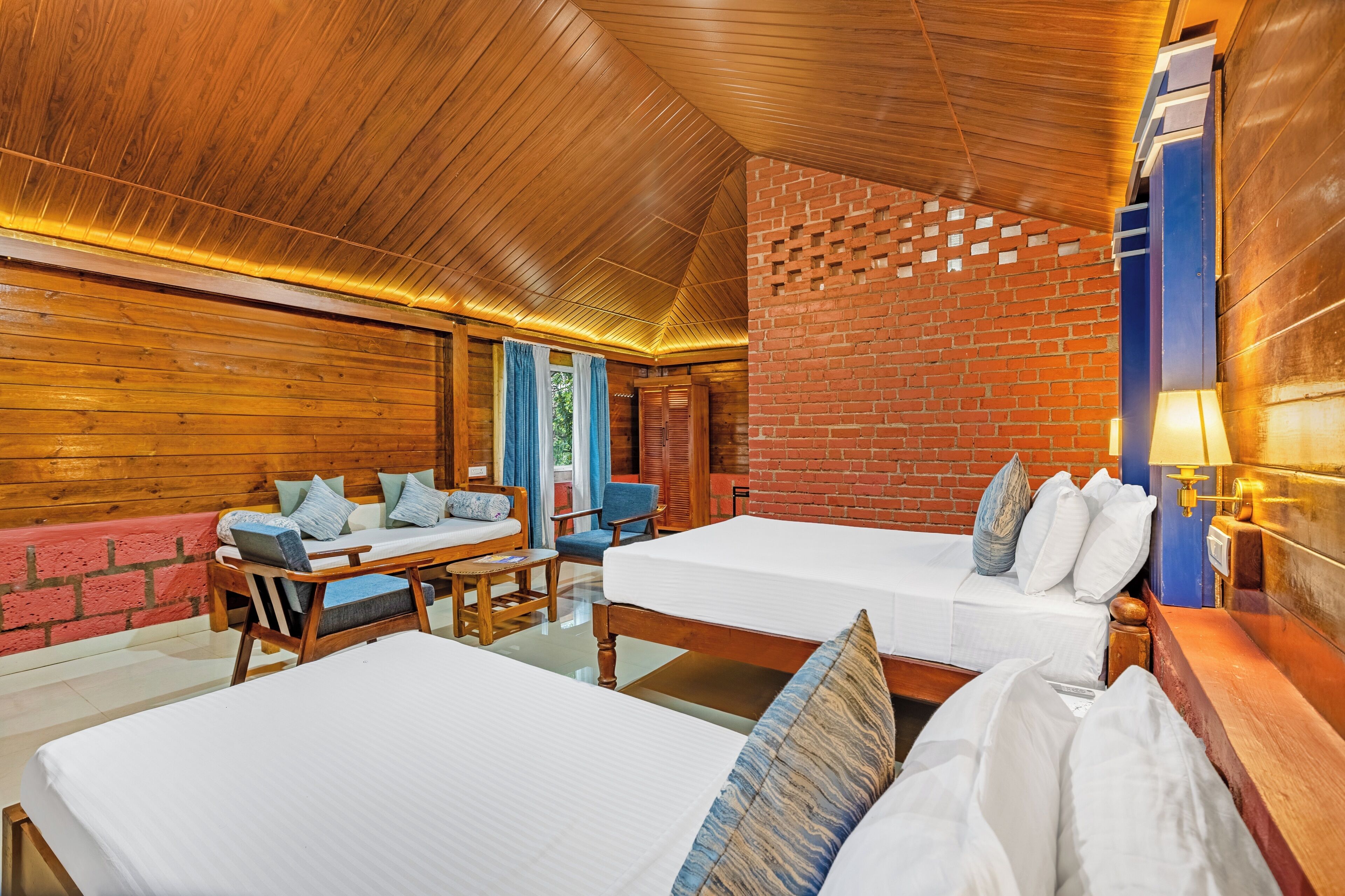 A room with two beds, a wooden ceiling, a brick wall, and a table with chairs.