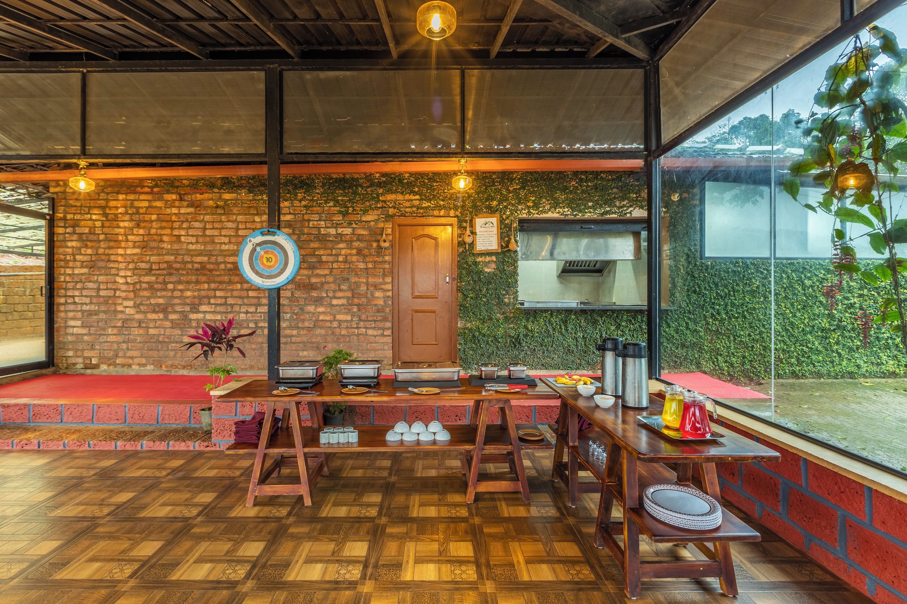 A dining area with a brick wall, wooden tables, and a view of a garden through large windows.