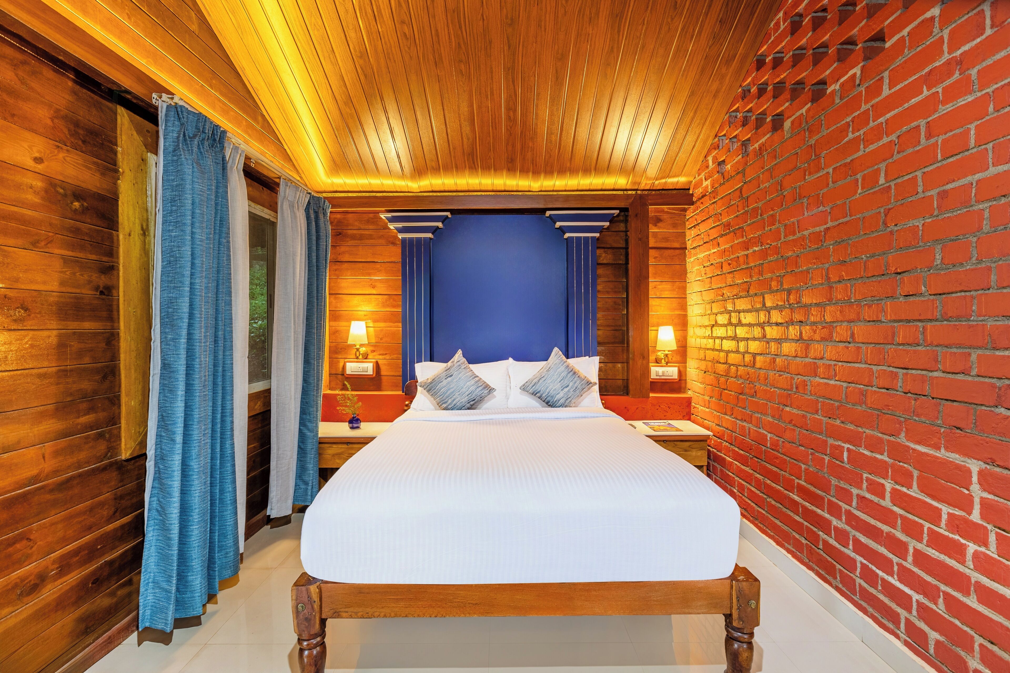A wooden-paneled room with a large bed, blue curtains, and two bedside lamps.