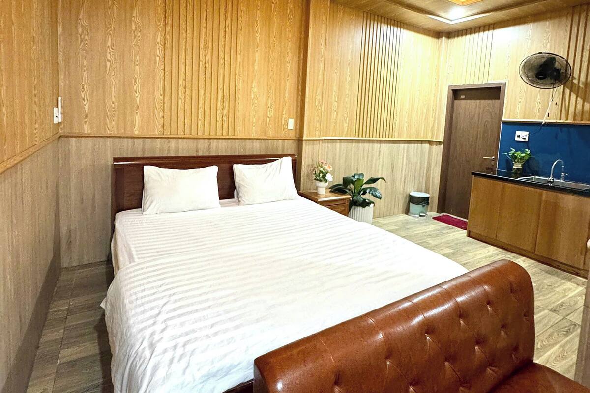 A hotel room with a bed, a wooden headboard, a desk with a chair, and a small plant.