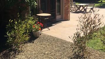 Un patio con una mesa y sillas, rodeado de plantas en macetas y un camino de grava.