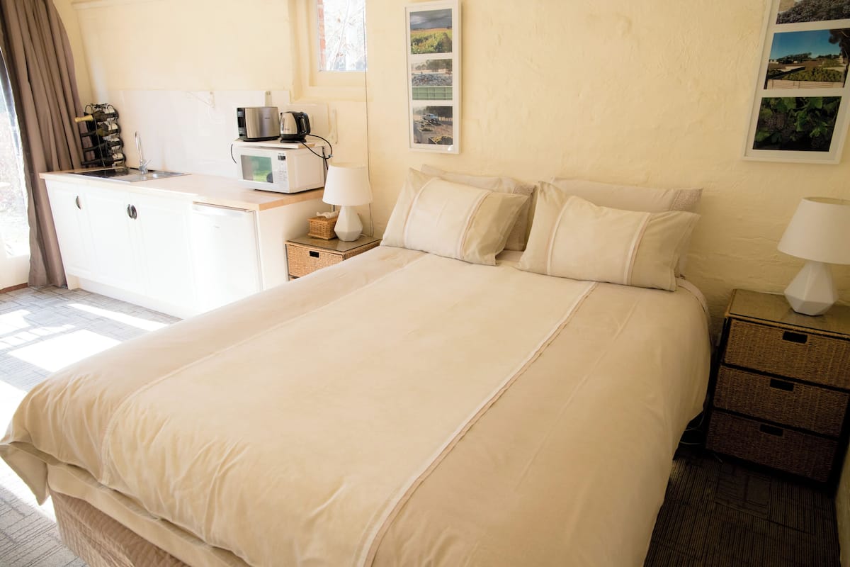 Habitación de hotel con una cama grande, un escritorio con microondas, cafetera y una pequeña mesa con lámpara.