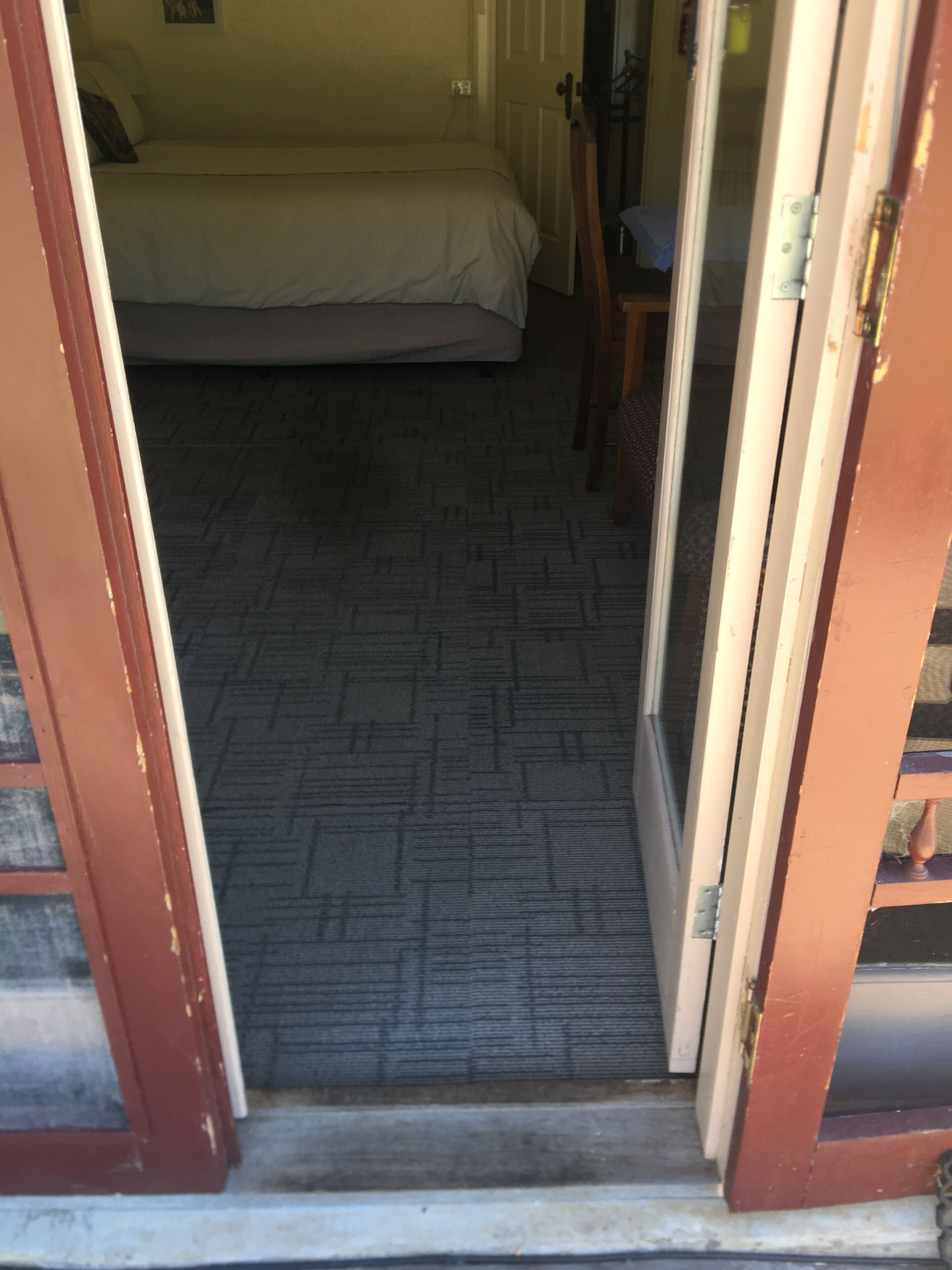 A narrow hallway leading to a bedroom with a bed and a door.