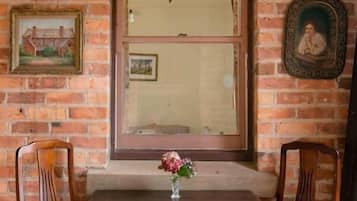 A dining area with a brick wall, wooden chairs, a table, and a vase with flowers.