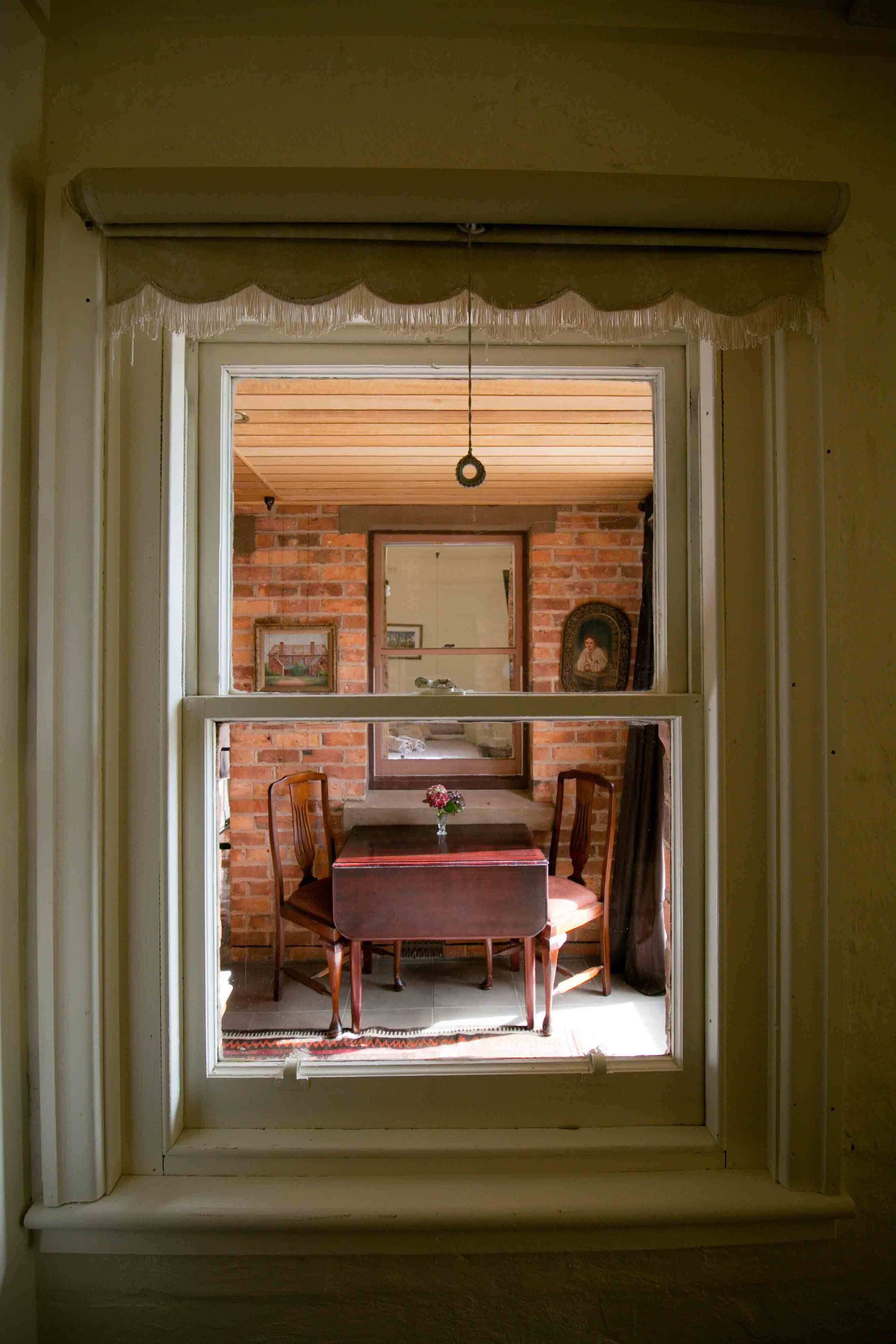 A room with a window overlooking a dining area, featuring a wooden table and chairs.