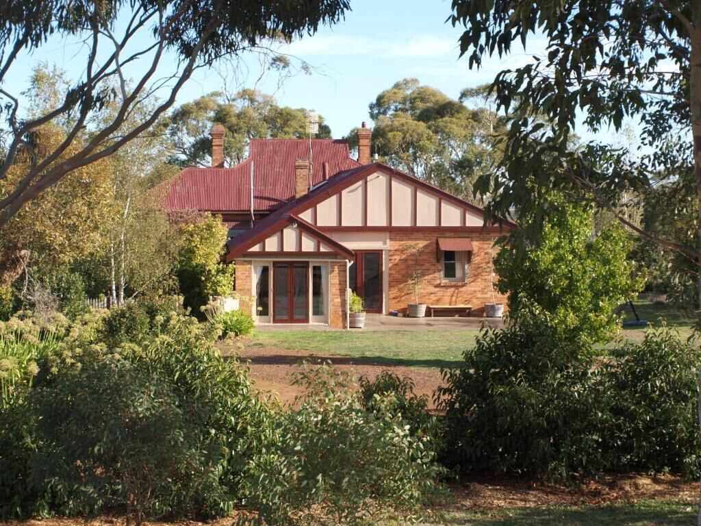 A two-story house with a red roof, surrounded by lush greenery and trees.