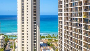Ein Hochhaus-Hotel mit mehreren Balkonen, Blick auf den Ozean und ein Strandgebiet mit Palmen.