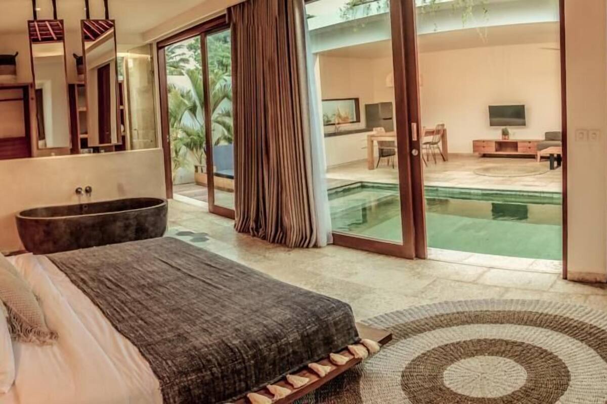 A bedroom with a large bed, a bathtub, and a view of a pool.