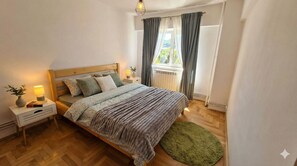 Ein Schlafzimmer mit einem hölzernen Bett, zwei Nachttischen mit Lampen, einem grünen Teppich und einem Fenster mit Vorhängen.