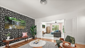 A modern living room with a stone-patterned wall, a round coffee table, and a view of a garden through an open door. - Stylish Home Near Stadium | Hot Tub, BBQ, Fire Pit (Baton Rouge)