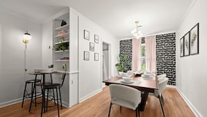 A dining area with a wooden table, white chairs, and a pendant light. There are shelves with books and plants, and a black and white patterned wall. - Stylish Home Near Stadium | Hot Tub, BBQ, Fire Pit (Baton Rouge)