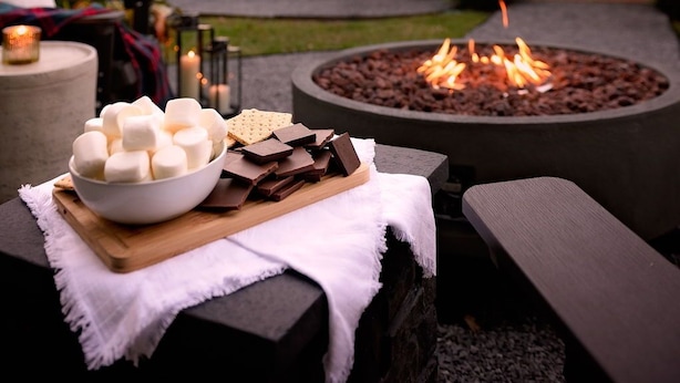An outdoor seating area with a fire pit, a bowl of marshmallows, and chocolate pieces on a table. - Stylish Home Near Stadium | Hot Tub, BBQ, Fire Pit (Baton Rouge)