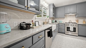 A kitchen with grey cabinets, a built-in oven, a microwave, and a blender on the counter. - Stylish Home Near Stadium | Hot Tub, BBQ, Fire Pit (Baton Rouge)