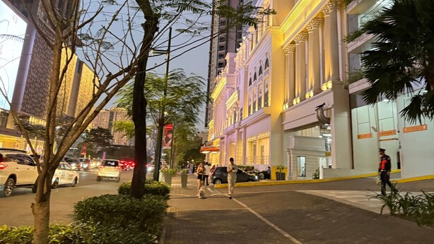 A street view with a building featuring a yellow facade and classical architecture, including columns and a balcony.