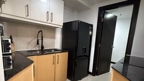 A compact kitchen with white cabinets, a black refrigerator, a sink, and a small mat on the floor.