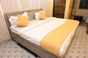 A bed with a grey headboard, white and yellow bedding, and a quilted blanket.