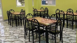 Un espace repas comprenant plusieurs tables et chaises, un sol à motifs et un mur vert agrémenté de fenêtres.