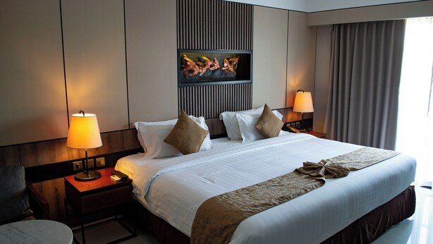Une chambre d’hôtel avec un grand lit, deux tables de chevet avec des lampes, une petite table ronde et un élément décoratif mural au-dessus du lit.