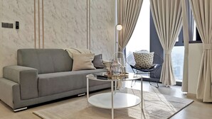 Ein modernes Wohnzimmer mit grauem Sofa, einem runden Couchtisch und einem Blick auf die Stadt durch große Fenster mit Vorhängen.