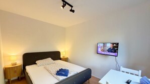 A bedroom with a bed, bedside lamps, a TV on the wall, and a small table with a chair.