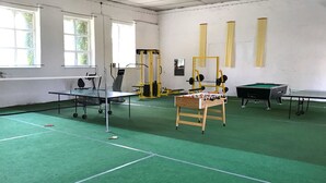 A sports hall with a ping pong table, foosball table, and weightlifting equipment.