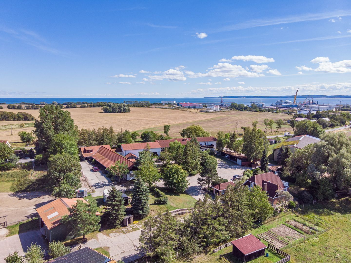 A residential area with houses, a large open field, and a port with ships and cranes in the background.
