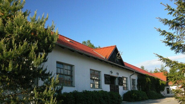 A white building with a red roof, surrounded by greenery.