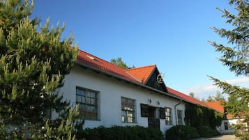 Ein weißes Gebäude mit rotem Dach, umgeben von viel Grün.